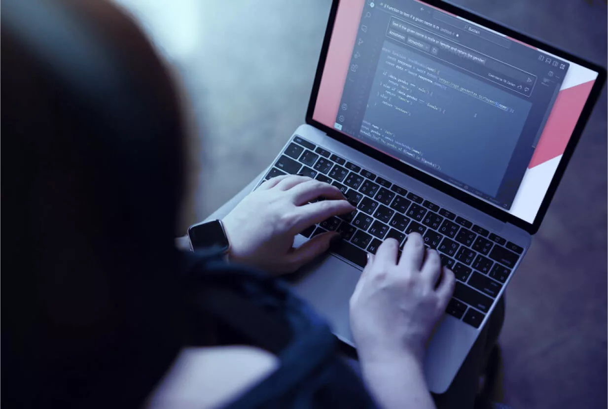 Person, die Code auf einem Laptop eingibt, auf dessen Bildschirm eine dunkel gestaltete Programmieroberfläche angezeigt wird.