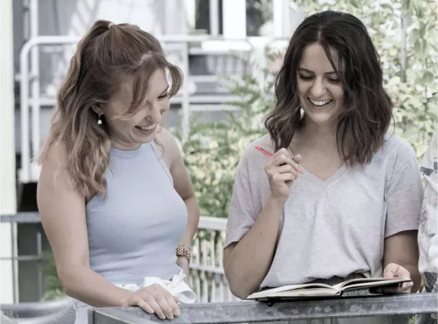 Zwei junge Frauen, blond und dunkelhaarig, die sich an einem sonnigen Tag auf der Dachterasse der Agentur zusammen amüsieren.
