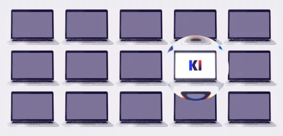 Zwölf Laptops sind in einem Raster angeordnet. Ein Laptop ist vergrößert dargestellt und zeigt auf seinem Bildschirm die Buchstaben „KI“ an.